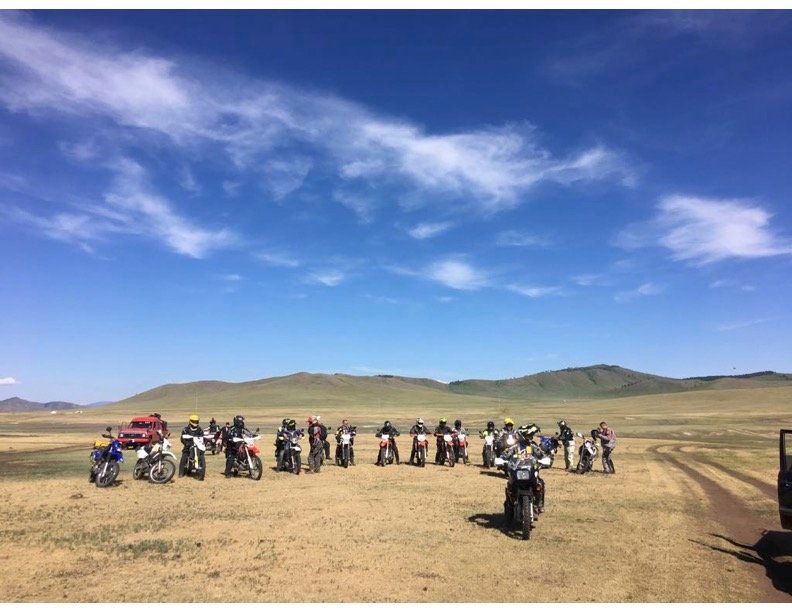 Group of riders and bikes gathered on open grassland under a wide sky