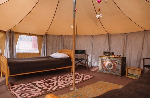 Single bed made up inside a mobile ger with a patterned rug and side table