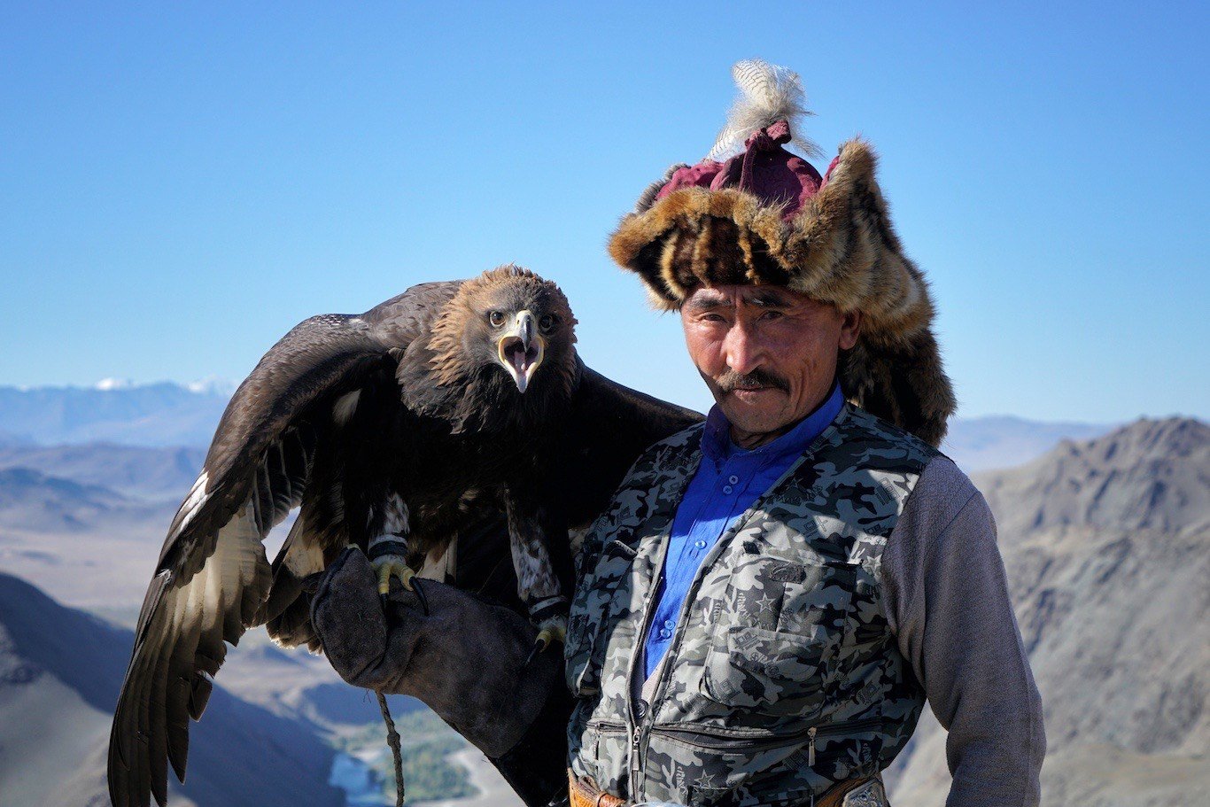 Kazakh eagle hunter Haizem holding his golden eagle above a mountain valley