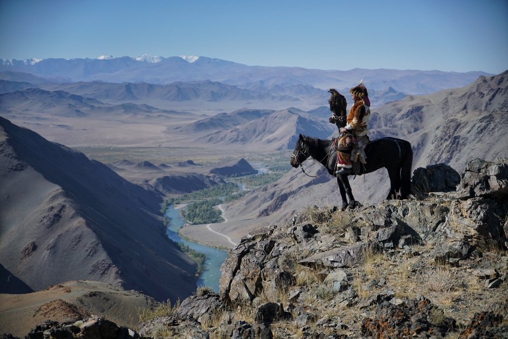 Eagle hunter on horseback on a ridge above a winding river