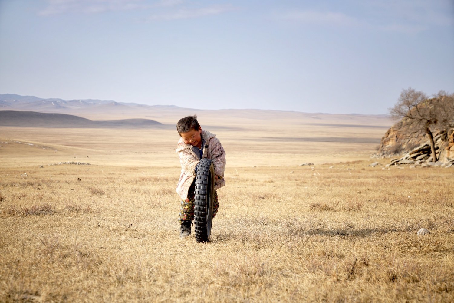 A child playing with a tyre on the open autumn steppe