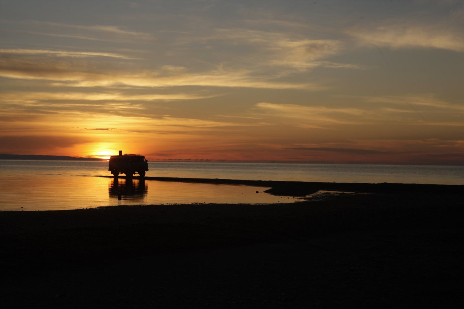 A UAZ expedition van silhouetted at sunset on the shore of a Mongolian lake